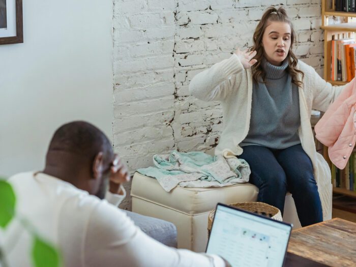 A man and woman arguing in a room while he looks at a laptop screen